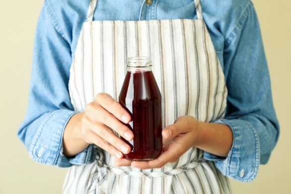 Une main soulève délicatement une grande mère de vinaigre avec une cuillère en bois au-dessus d’un récipient