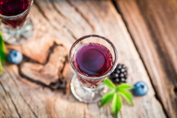 Une personne mélange doucement les feuilles et les baies dans un récipient en verre avec une cuillère en bois, sous une lumière naturelle