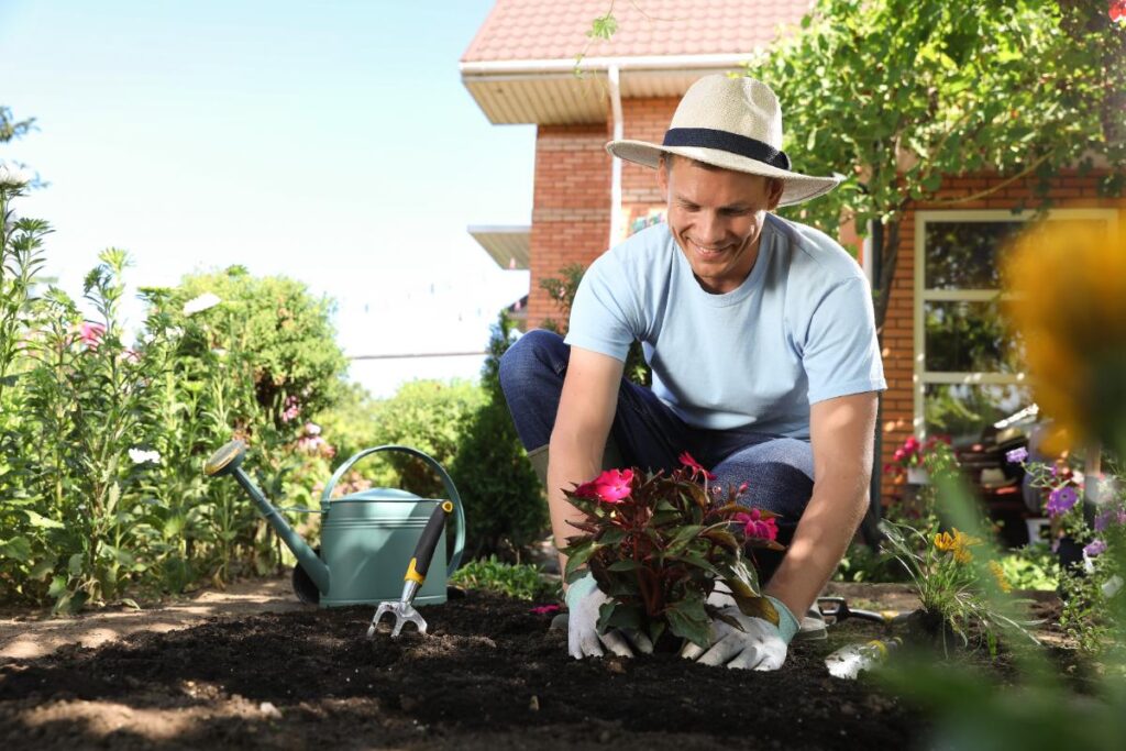Un homme en chapeau plantant de belle fleurs dans le jardin